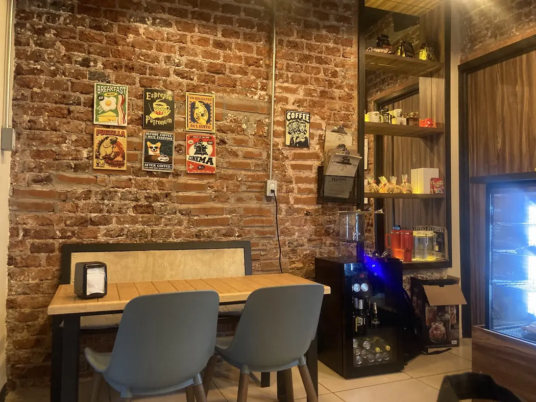El interior de The Latte Date, con mesas de madera y una cálida pared de ladrillo